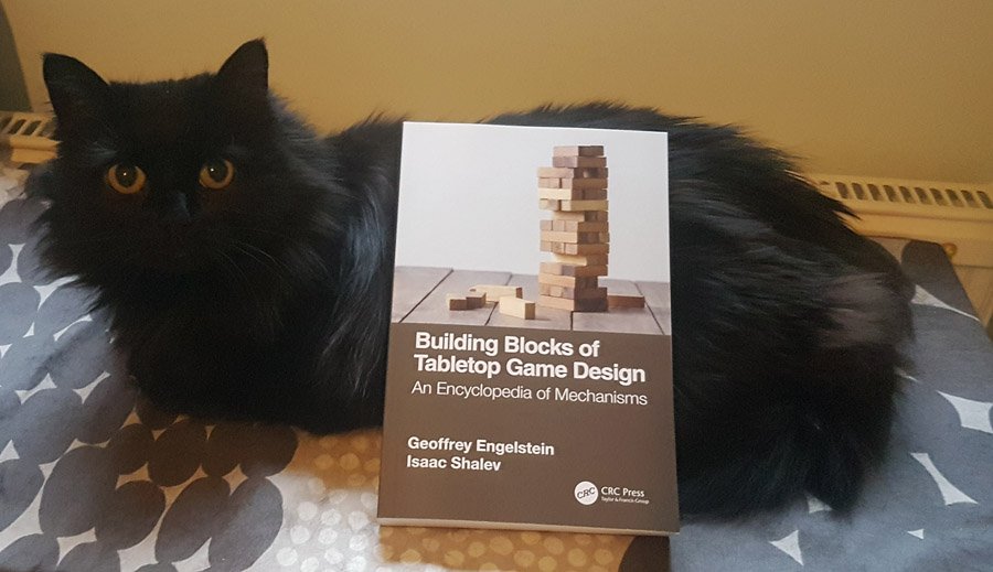 Otava the cat posing with Geoffrey Engelstein's and Isaac Shalev's book ”Building Blocks of Tabletop Game Design”.