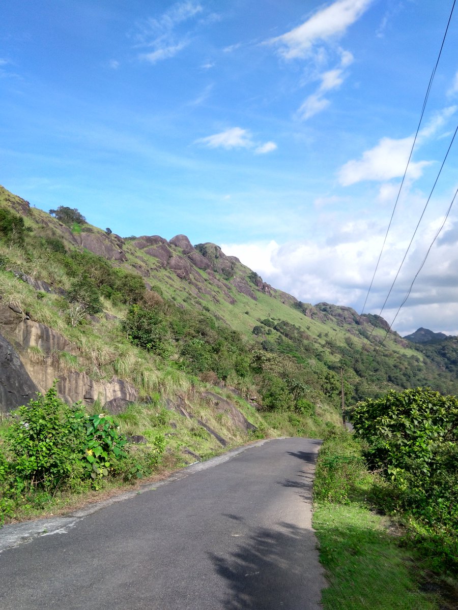 KeralaTourism's tweet photo. Soft little clouds form against the clear blue skies of Vagamon. Dense greens line the sides of the smooth tarmac. Rocks and boulders stand erect, like silent keepers of a less explored land. https://t.co/FlYzjmi3Wh