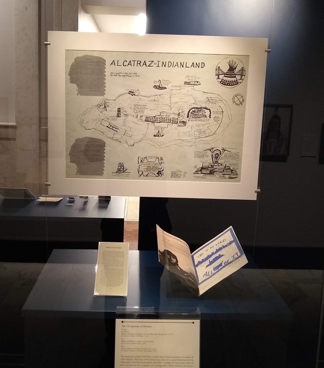 Map entitled "Alcatraz-Indianland," hanging above a small handbill entitled "Alcatraz Is Not an Island" and a spread of a periodical issue with drawing of Alcatraz Island entitled "This Is My Land/All of It"