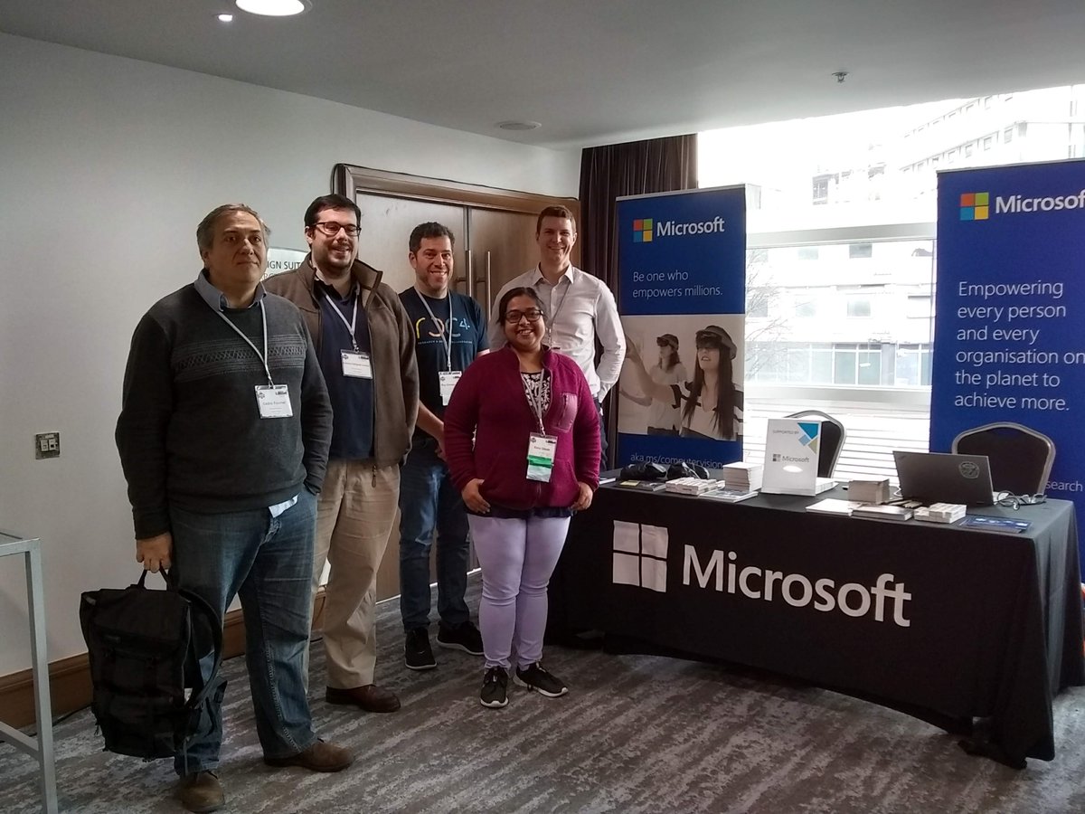 A line of people smiling at the camera stand in front of the Microsoft table at CCS.