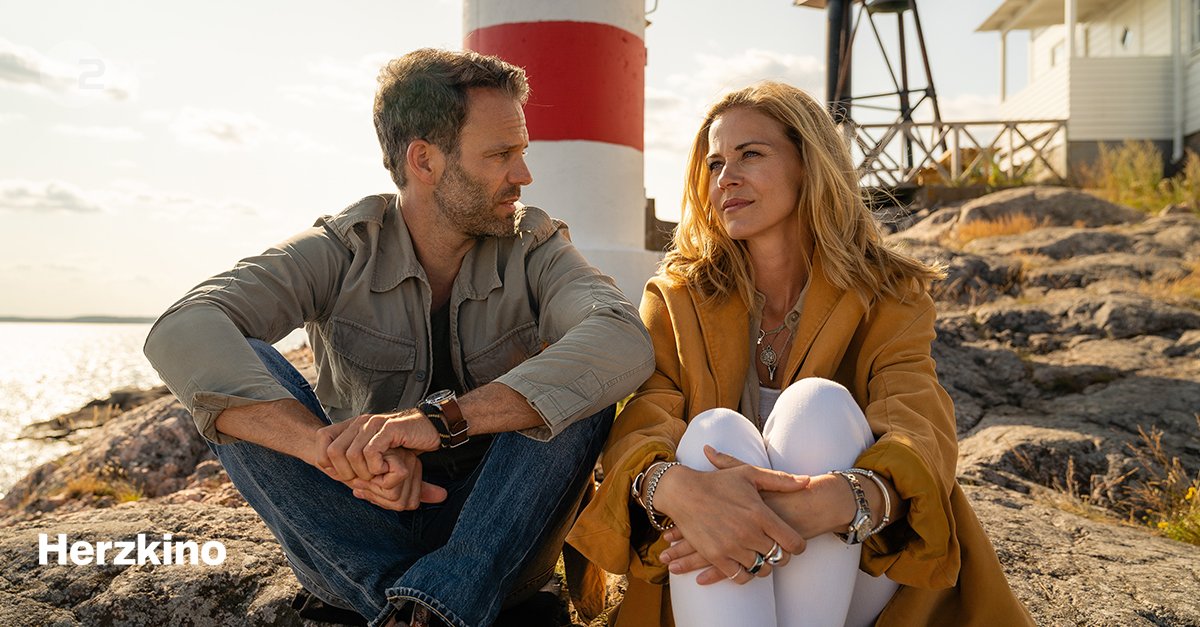 "Inga Lindström: Familienfest in Sommerby": Tilda (Jessica Ginkel) und Lasse (Ben Ruedinger) sitzen auf einem Felsen am Meer. Lasse sieht Tilda an, die in die Ferne schaut. Im Hintergrund sind ein kleiner Leuchtturm und ein Haus zu sehen. Sonntag, 20:15 Uhr im ZDF.