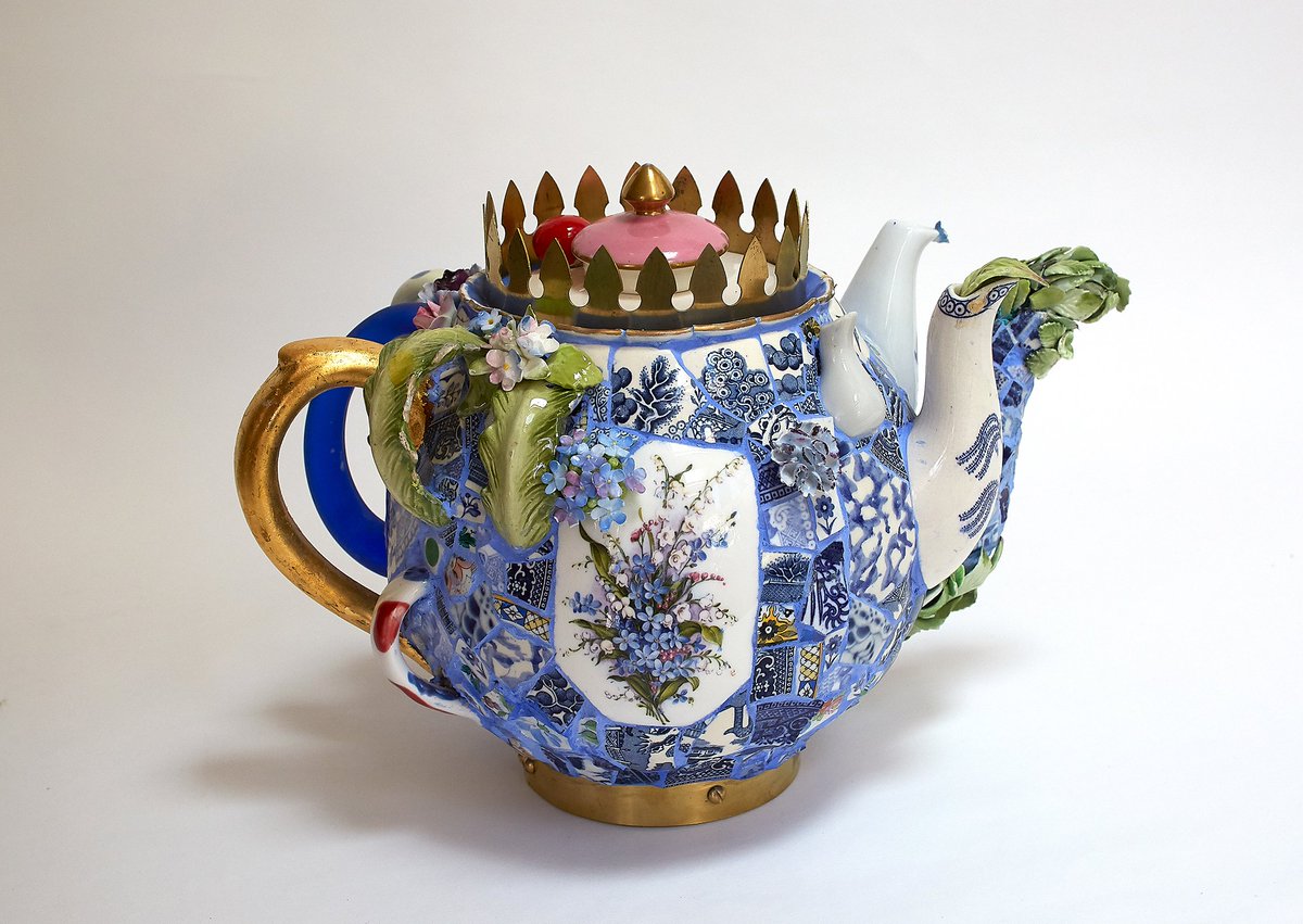 [image description: a teapot by Candace Bahouth, a white teapot covered in blue and white mosaic tile, the pot has two spouts and four handles, at the top of the pot as well as the pink and gold lid there is a crown on the circumference surrounding it.]
