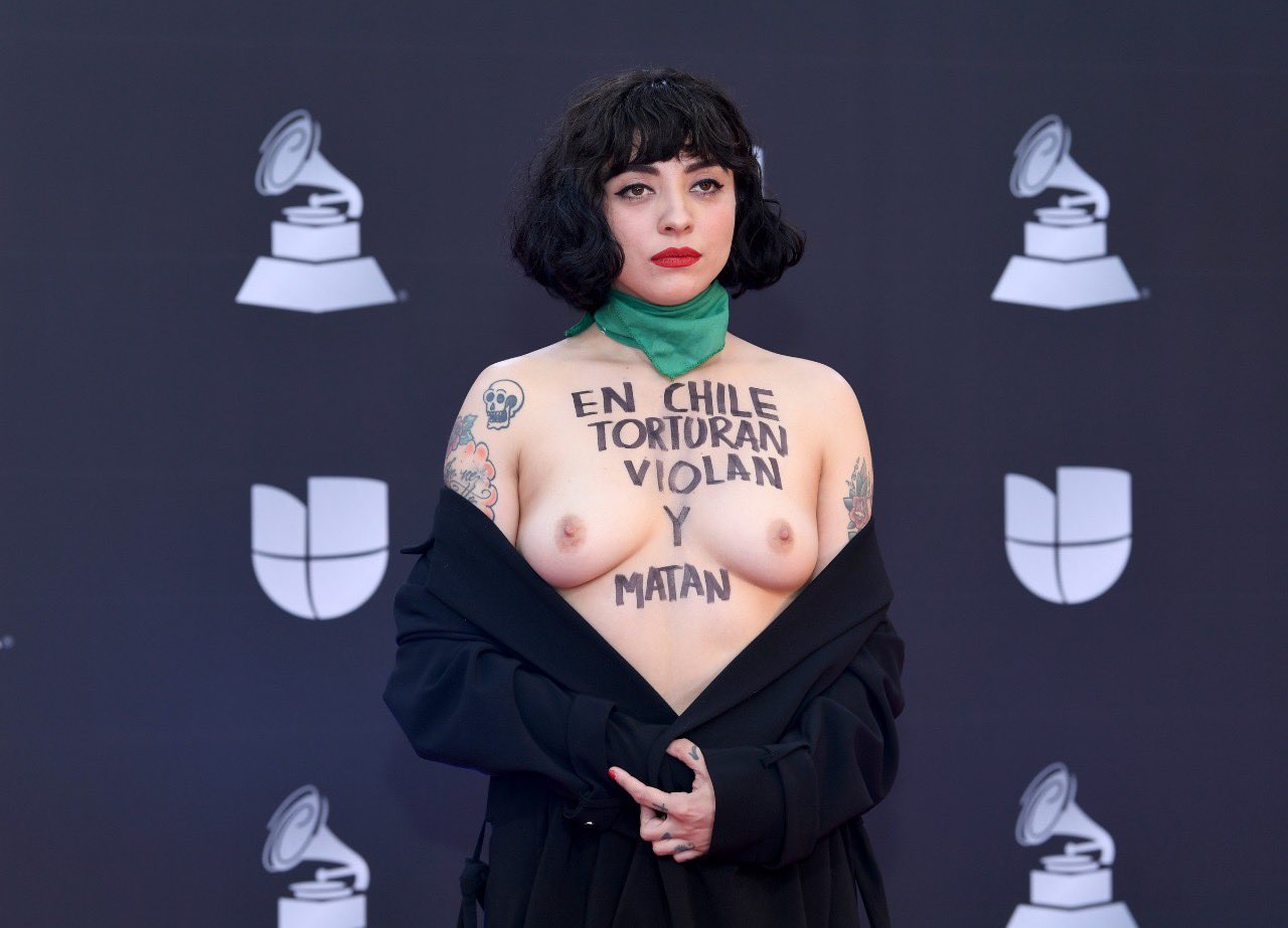 Mon Laferte en los Latin Grammy con el torso desnudo donde se lee 