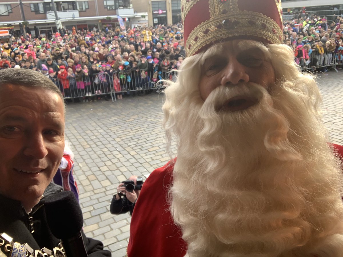 Een selfie met Sinterklaas met enthousiaste kinderen en hun ouders op de achtergrond over zijn komst.