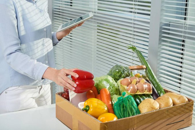 A woman picking up a pepper from a box of groceries. 