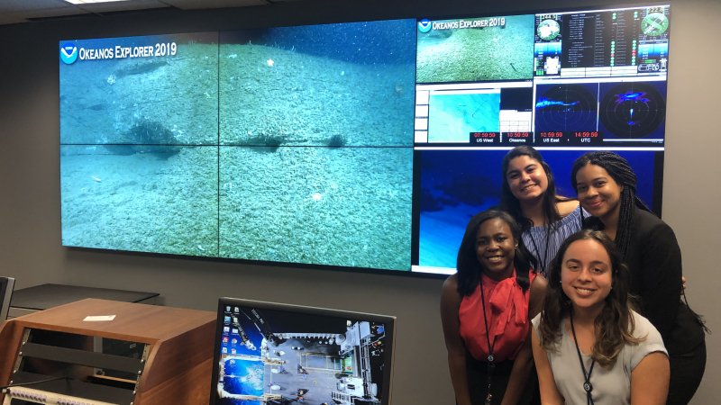 Scholars pose next to a screen with marine life.