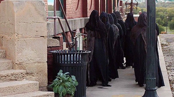 MondayAt1101AM's tweet photo. People with hoods and robes are walking down the street during the day carrying something. No one seems to notice except Michael #CharlesAgron in #MONDAYAT1101AM https://t.co/ezl7rgeTel