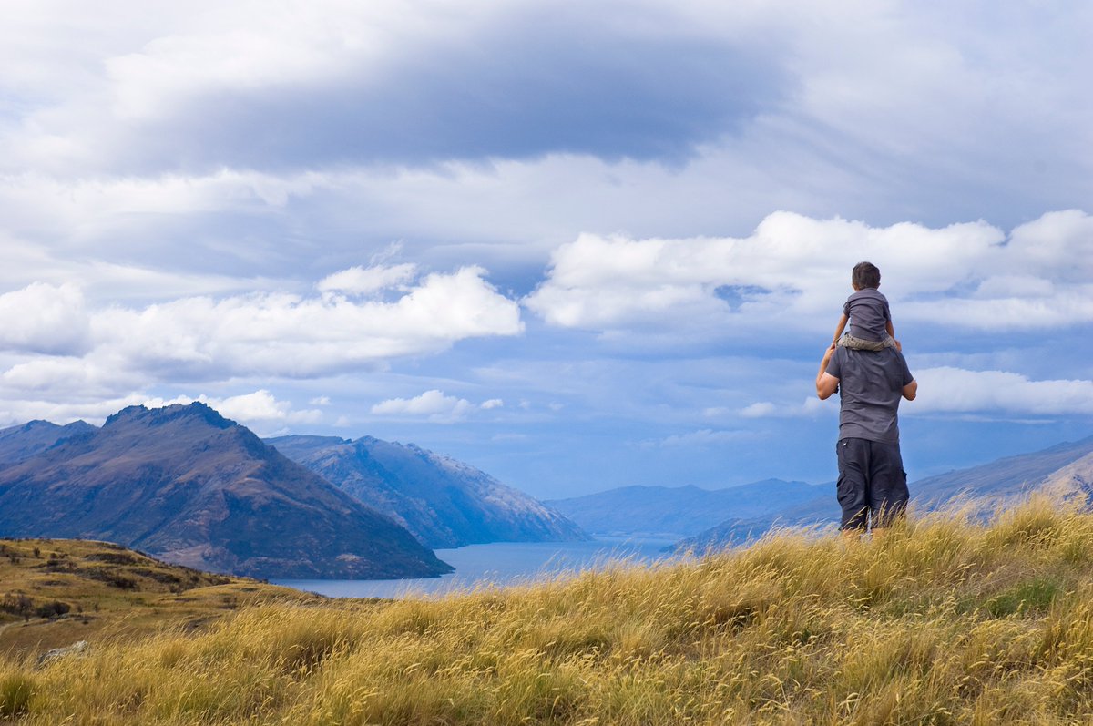 a man with his son on his shoulders in front of a scenic mountain range