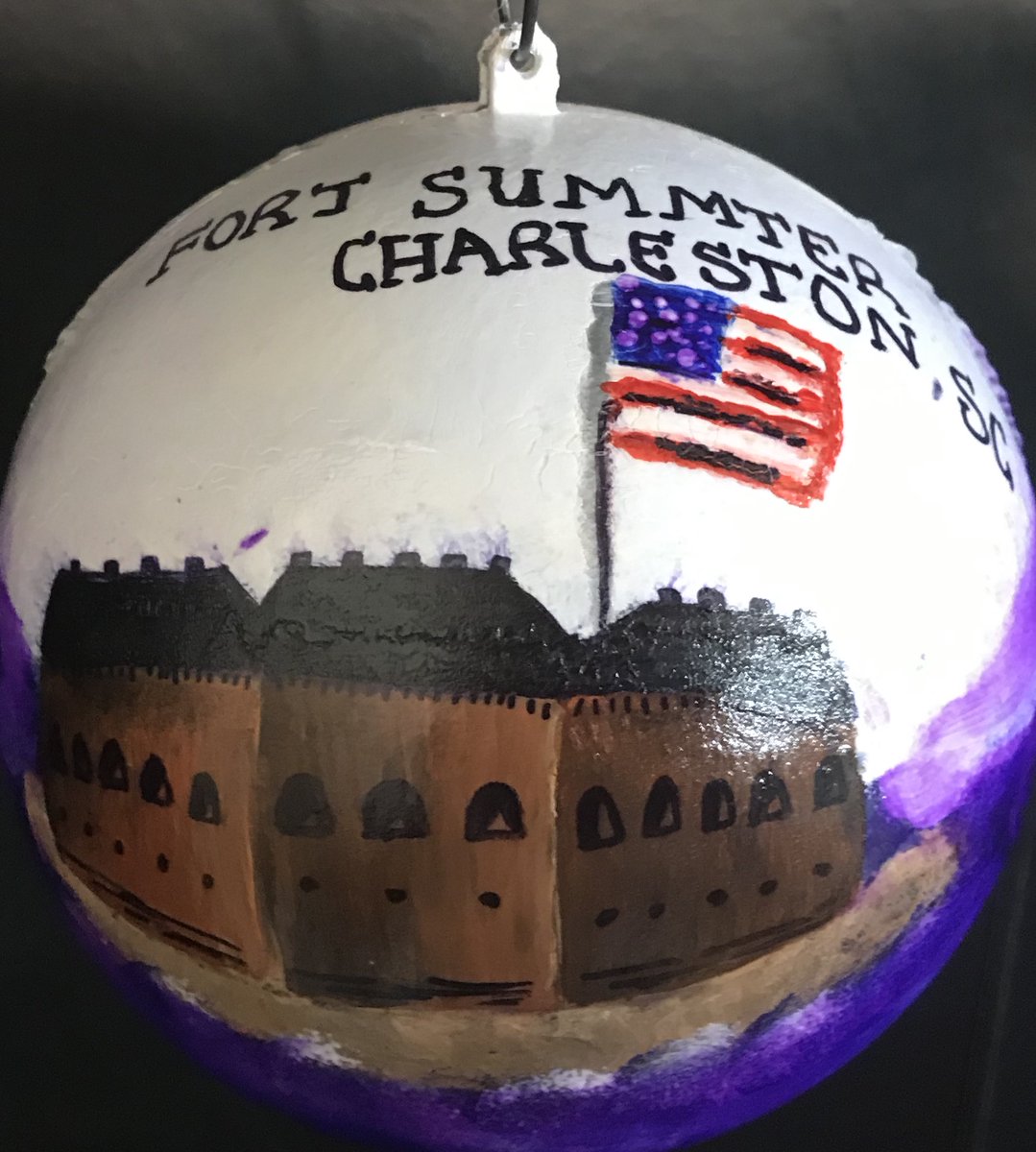 ornament of white and purple background colors with a brown fort with a US flag flying above it. Words above flag say "Fort Sumter Charleston, SC