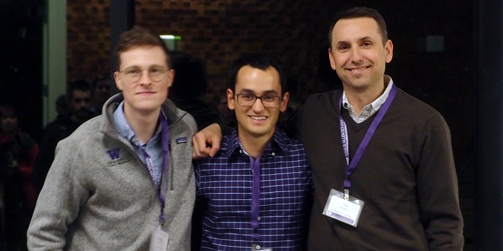 Three people smiling with arms around shoulders