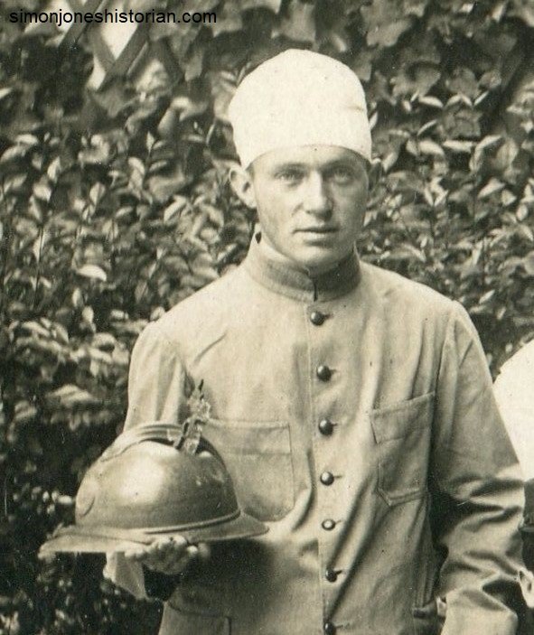 This man displays the large shell splinter still embedded in his steel helmet.