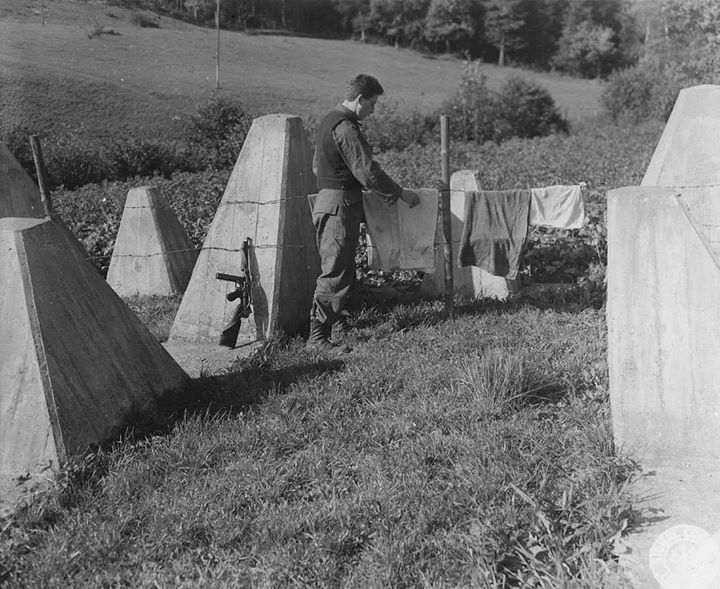 WarHistoryOL's tweet photo. What was intended to be a formidable trap for advancing allied armies turns out to be an excellent place to dry washing. PFC Anthony Mesinko, Cleveland, Ohio, uses the barbed wire of the 'impregnable' Siegfried Line to hang out his clothes https://t.co/PvI7y3MLoS