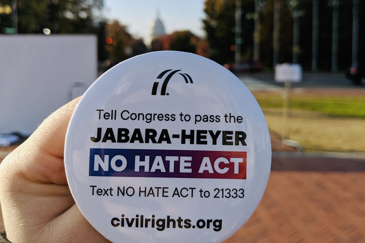 A button is held in Washington, DC with the U.S. Capitol visible in the background. The button reads "Tell Congress to pass the Jabara-Heyer NO HATE Act. Text NO HATE ACT to 21333. civilrights.org"