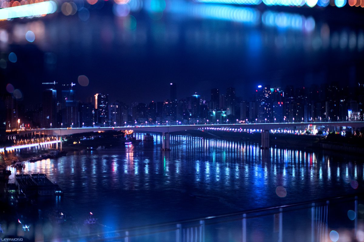 Photography by Liam Wong of Chongqing, China at night. A wide photograph of a bridge surrounded by bokeh. It Is blue in color.