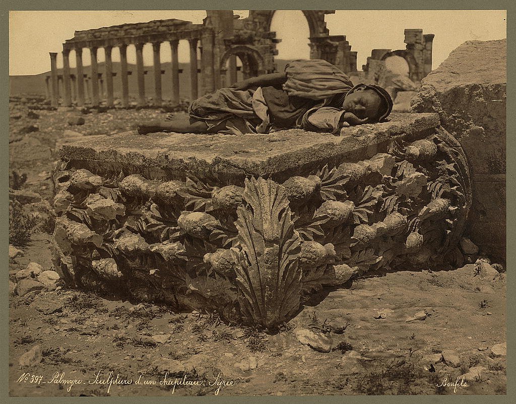 An old man sleeps on a fallen acanthus capital with the colonnade of Palmyra in the background, Syria c.1867 photograph by Félix Bonfils.