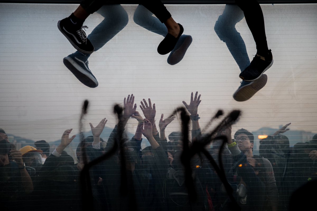 I don’t normally post photos on twitter, but I can’t stop thinking about this one I took: protesters climbing over fence, painted w “HK,” to avoid arrest, and their comrades catching them from the other side. Dark as hell, rosy as heaven. #HongKong
