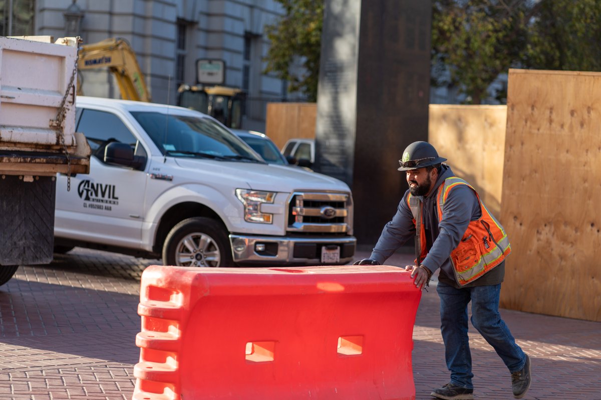 construction worker pushes orange plastic barrier around