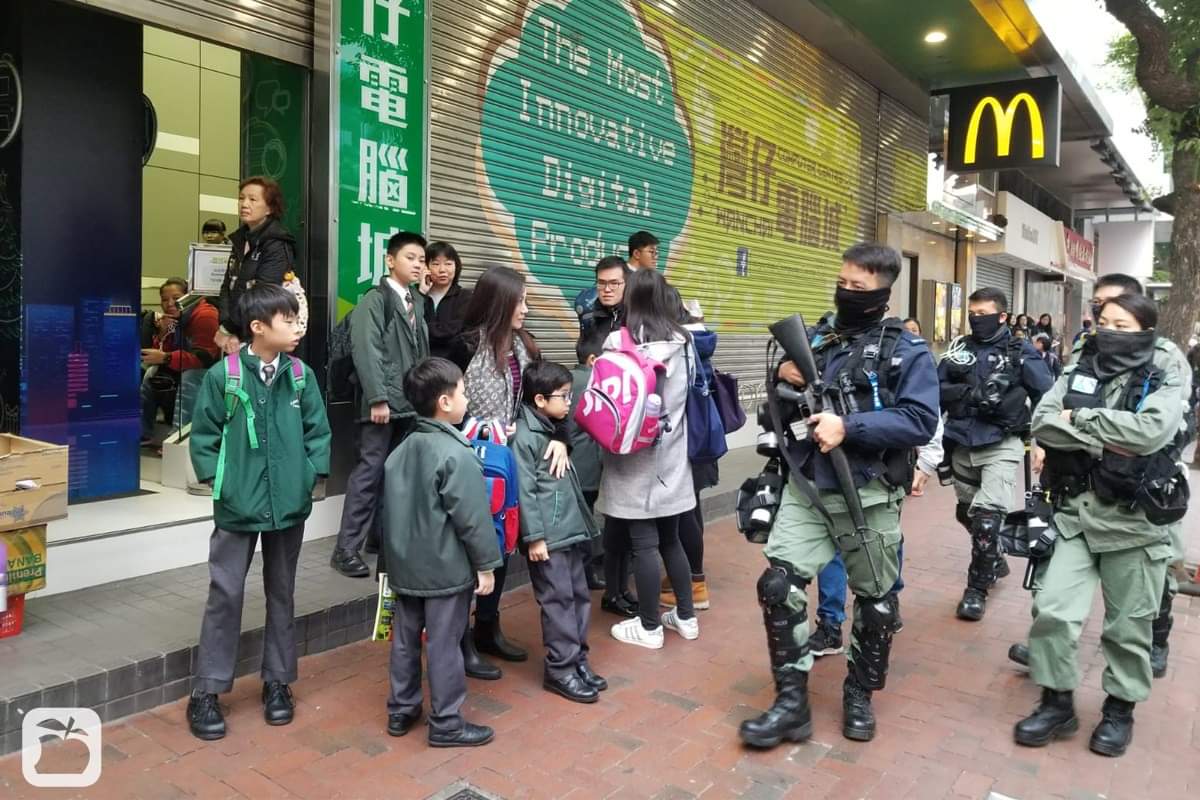 Tritri_zia's tweet photo. A picture speaks a thousand words. Can you see the fear in the eyes of the children and parents? Is a gun needed on a street crowded with students? No one feel safe when seeing the #PoliceTerrorist!  
Photo: @appledaily_hk 

#HKPoliceBrutality #HKPoliceState  
#FightForFreedom https://t.co/n6PUDQWqyO