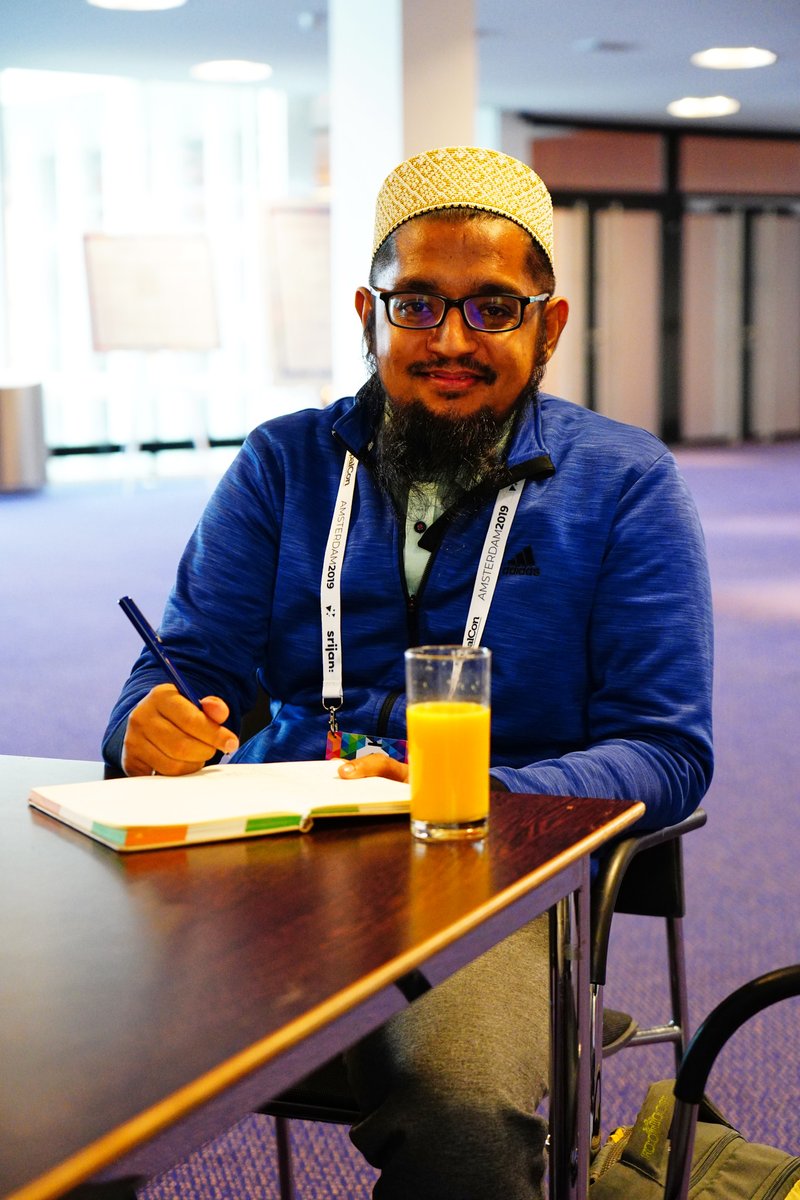 Taher sitting indoors writing things for his talk with a glass of juice on the table.