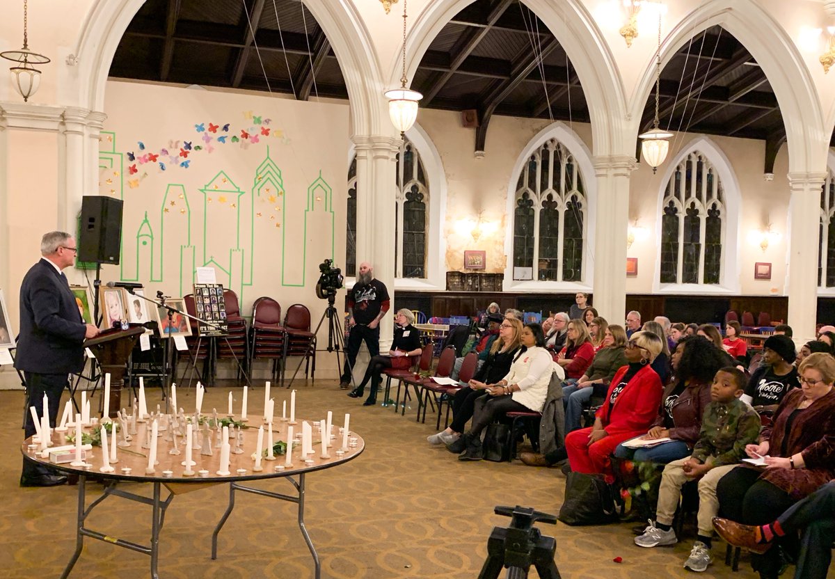 Mayor Kenney speaking to residents at vigil. A table with candles for the lives lost to gun violence is next to him.