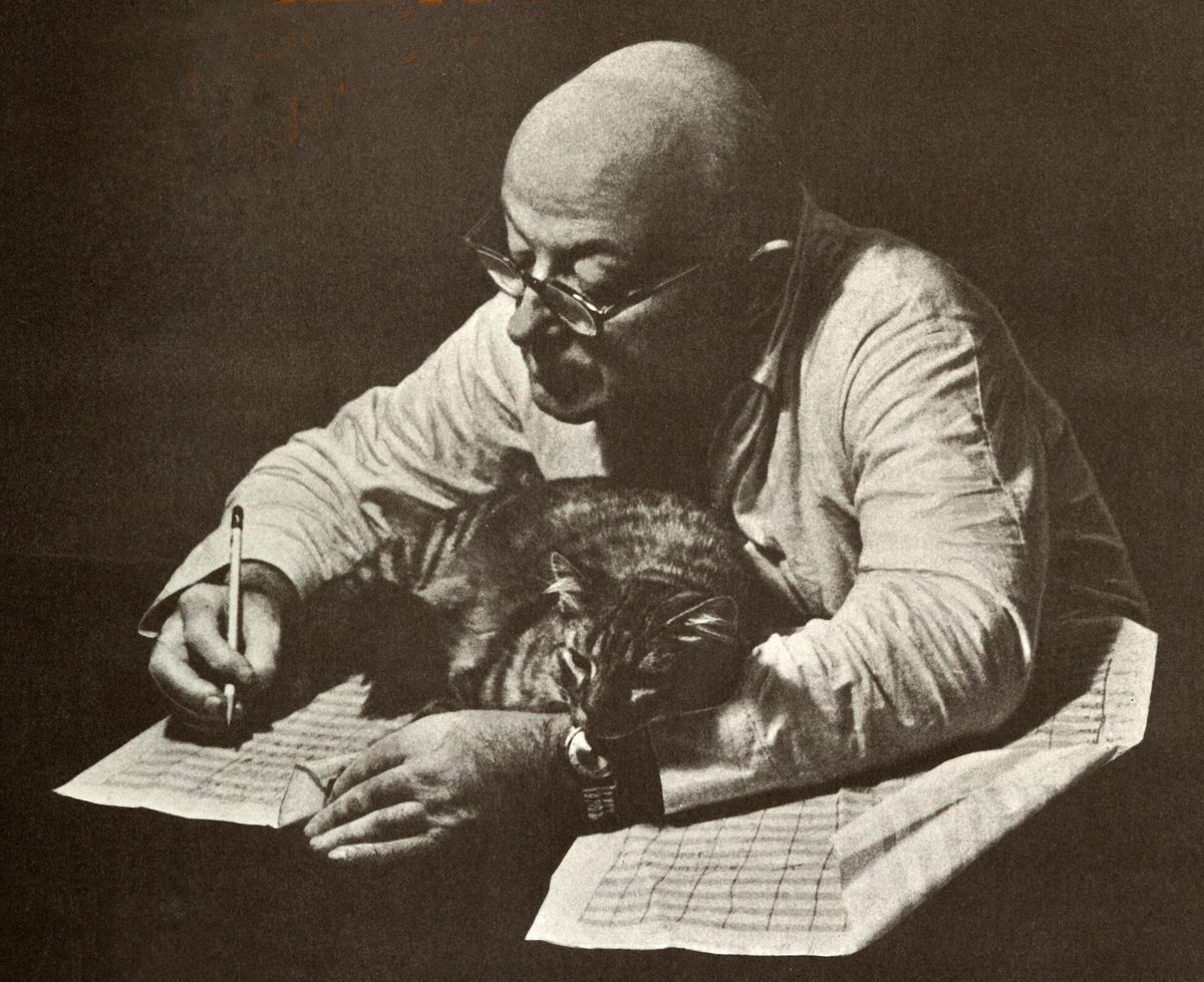 composer Henry Cowell at a desk writing music with a cat napping on the paper