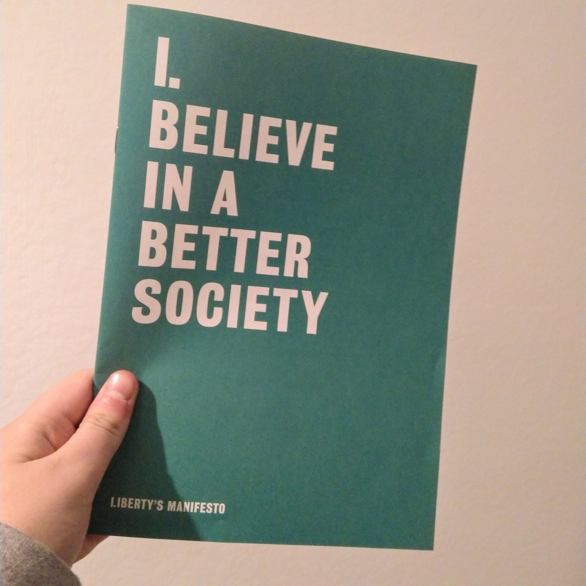 Photos of Liberty's election manifesto held up against a white background. It is green with the words "I believe in a better society" in white capitals