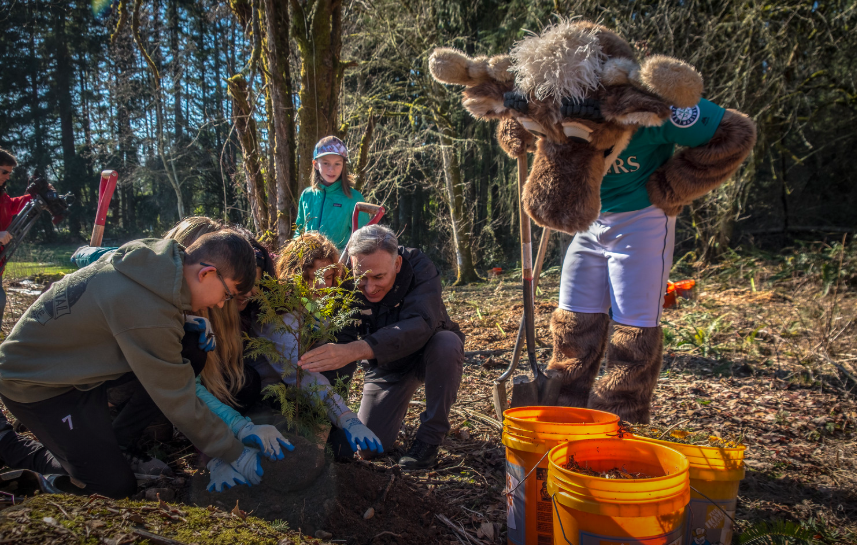 Executive Constantine helps some kids plant a tree while the Mariner Moose looks on.