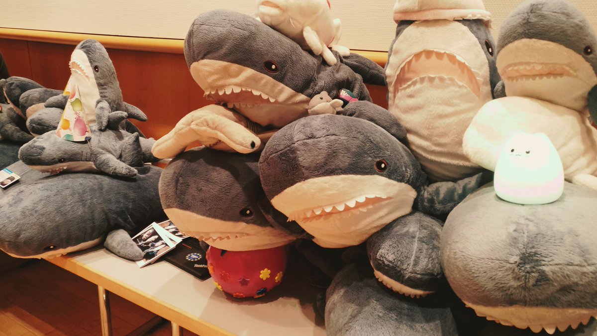 A pile of sharks and other fish plushies on a table, decorated with hats and other stuff.