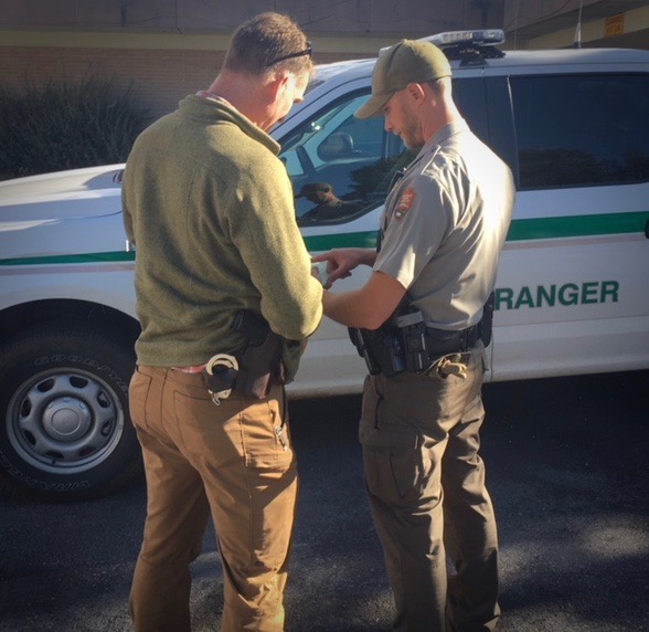 A Special Agent and a US Park Ranger confab next to a ranger vehicle.