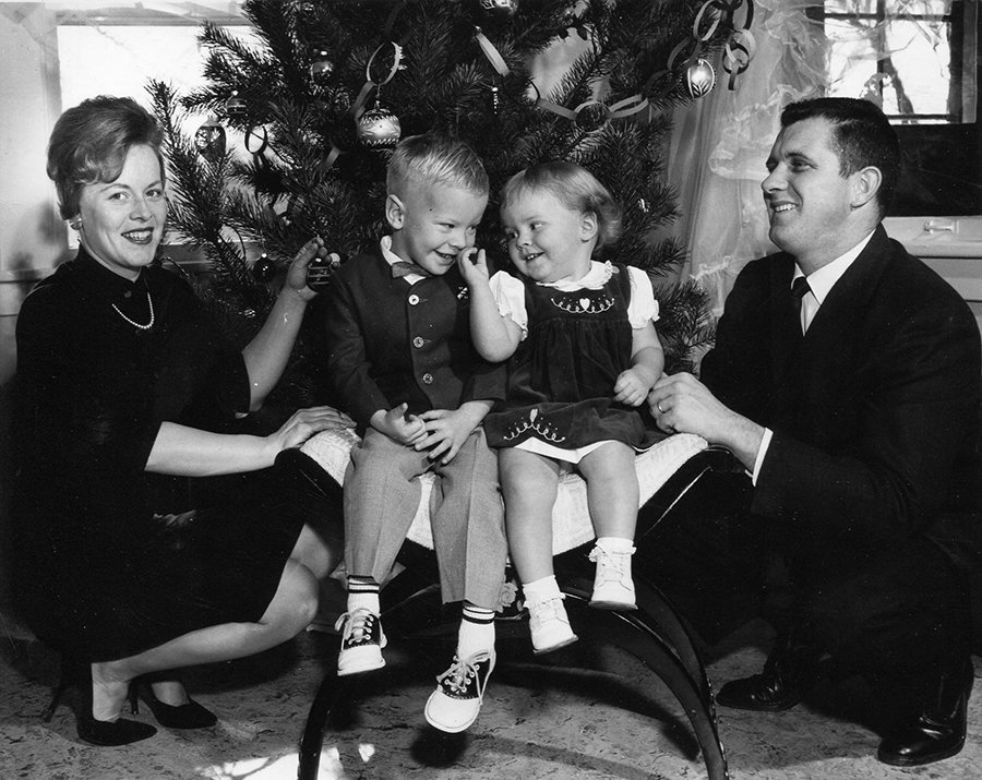 a man and woman from the 1960s in front of a Christmas tree kneeling next to two smiling young children