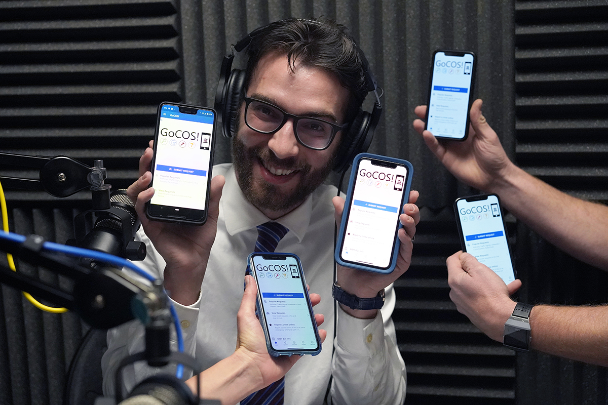 Podcast host Ted Skroback surrounded by cell phones with the app's homepage visible.