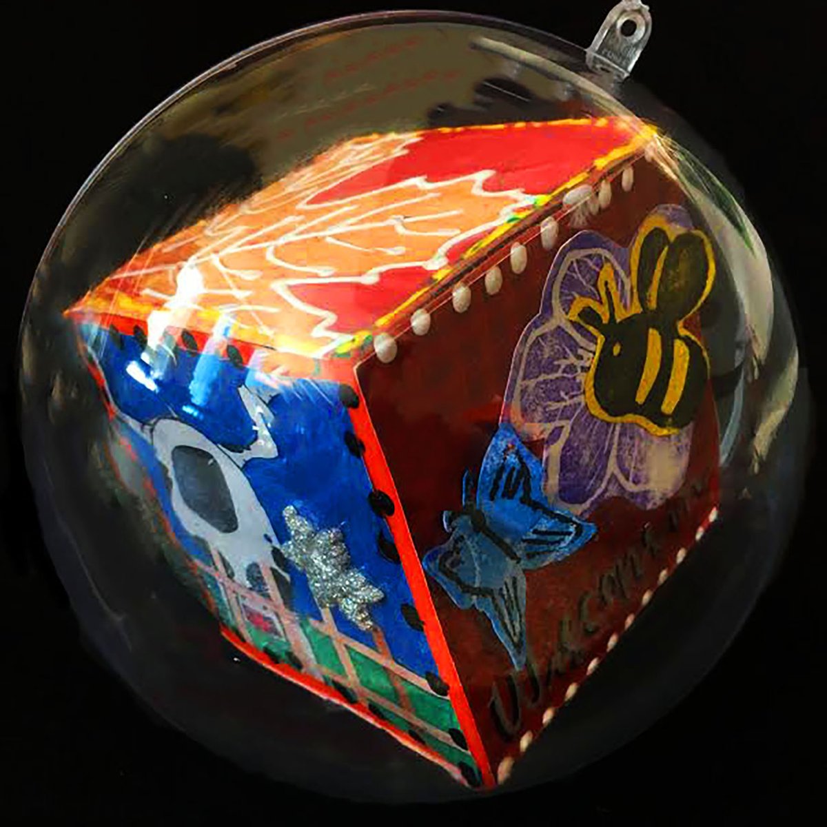 cube inside of an ornament; three sides are visible - one has a dairy cow, one has a leaf, and the other is of a butterfly and a bee with the word Wisconsin