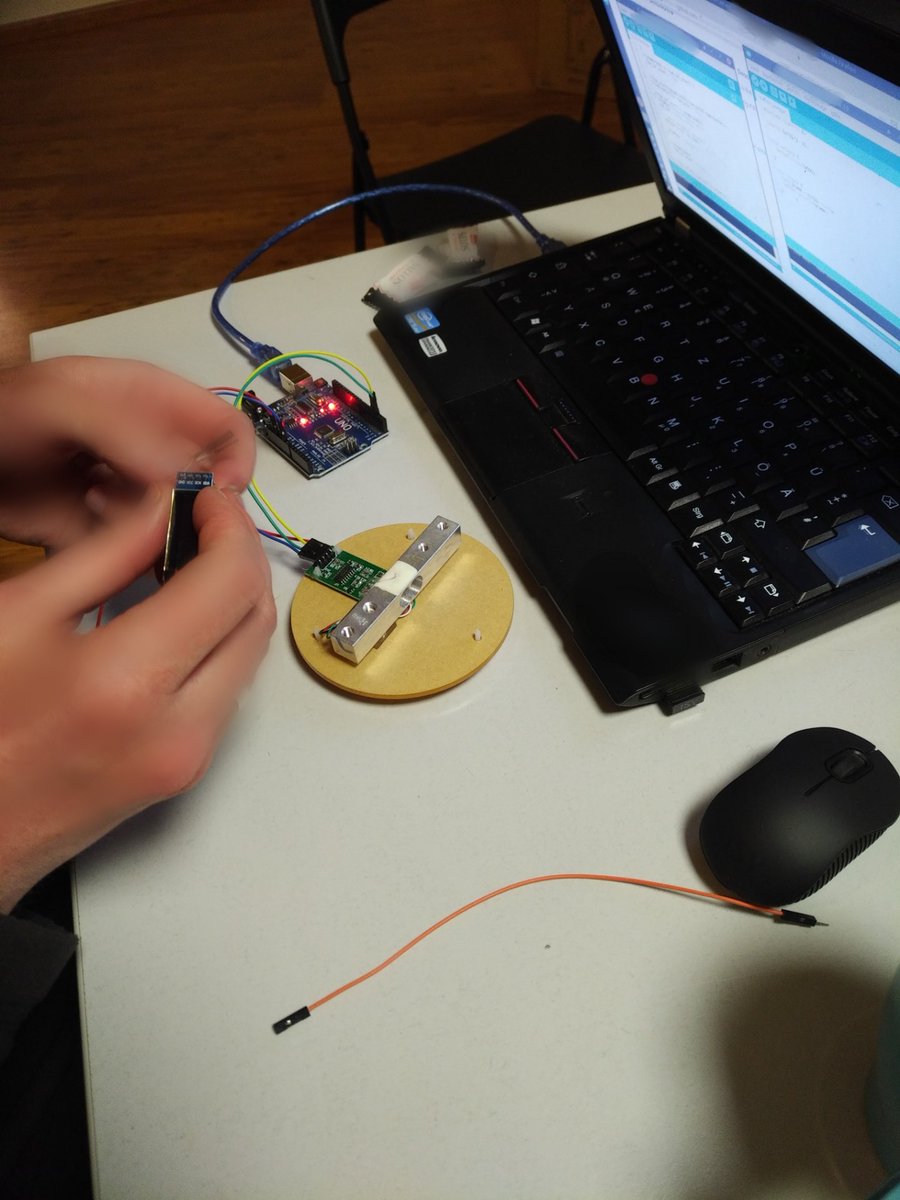 An einem Elektronik arbeitende Hände vor einem Laptop. Die Elektronik scheint ein Arduino Uno und eine Wägezelle zu sein. Auf dem Bildschirm ist nicht näher definierter Code zu sehen.