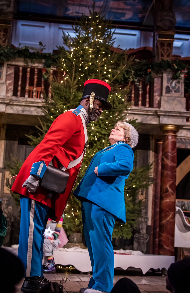 An actor dressed as a toy soldier leans over an actor in a blue suit.
