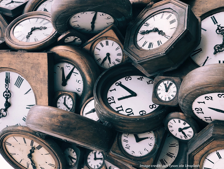 Disorderly pile of brown and white clocks, all showing different times. Photo credit: Jon Tyson via Unsplash.