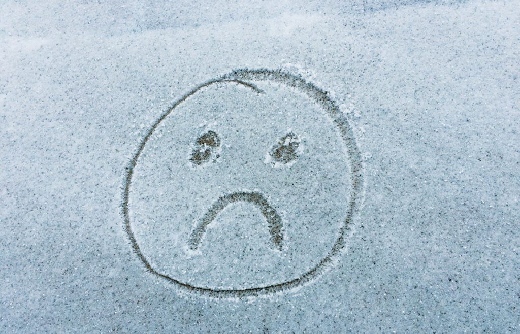 A sad face written in the frost on a windshield by someone's finger