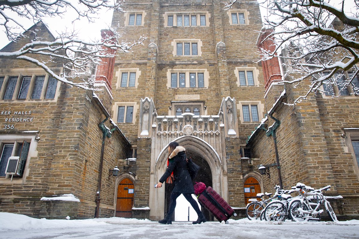 young woman pulls luggage in front of a snow-covered Baker Tower at Cornell University