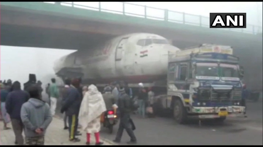 ANI's tweet photo. West Bengal: A truck carrying an abandoned India Post aircraft has got stuck under a bridge in Durgapur. More details awaited. https://t.co/jGXkOuTqHs