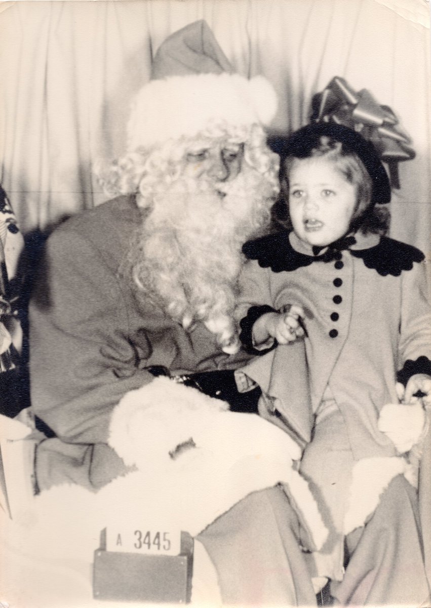 A young Elizabeth Warren takes a photo with Santa Claus, looking mildly terrified.