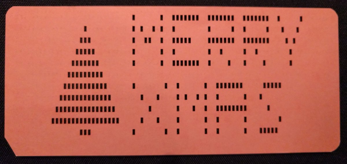 A punch card with the hole pattern spelling out MERRY XMAS, along with a Christmas tree.