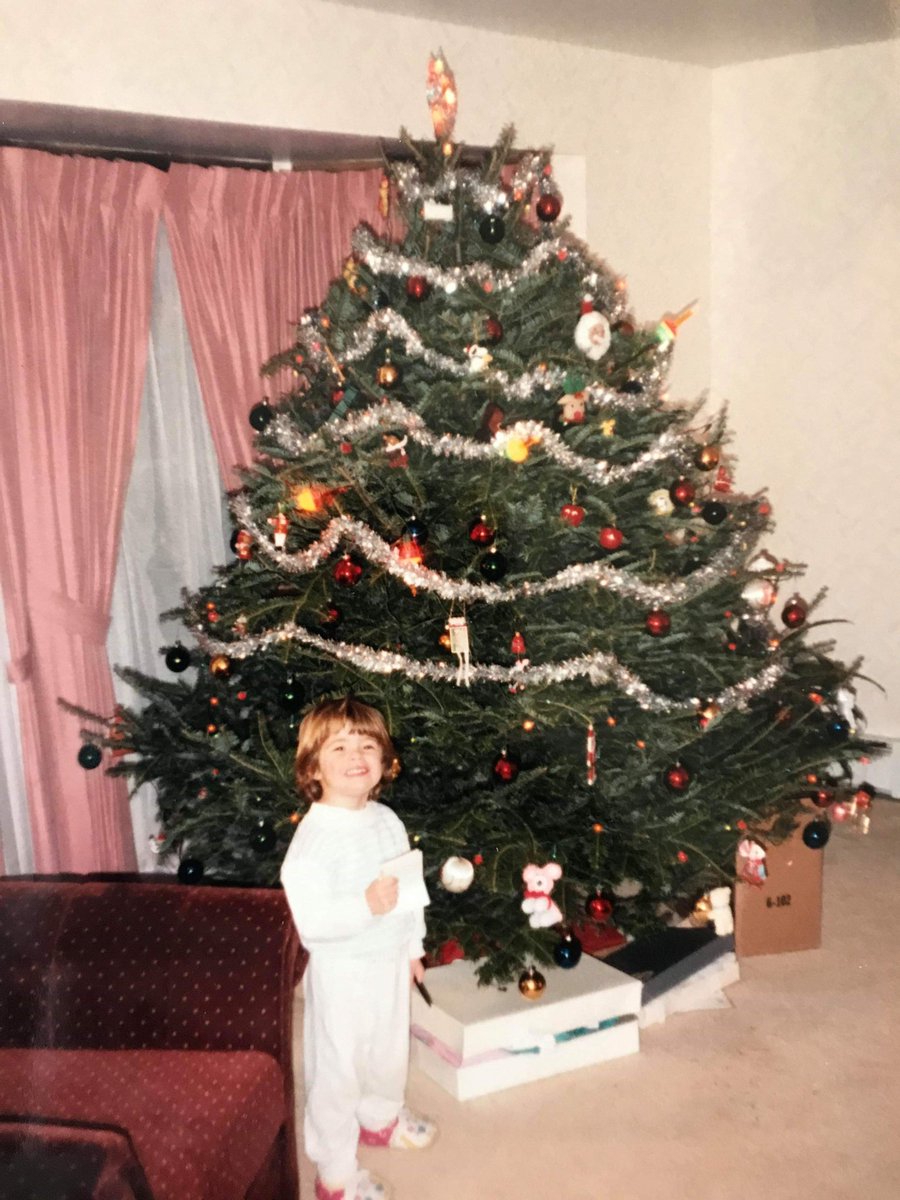 Jess as a child standing in front of a Christmas tree.