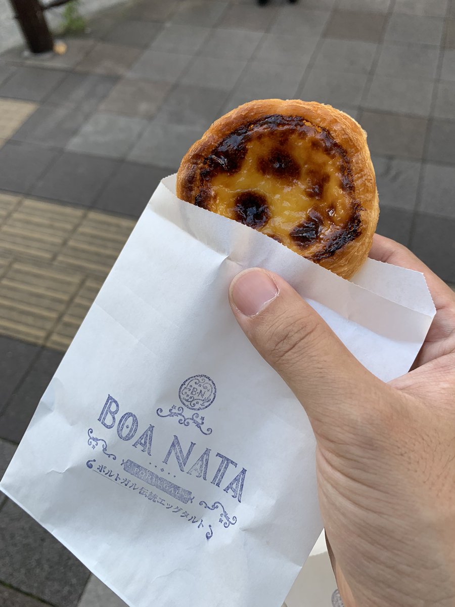 持ち歩き用紙袋からエッグタルトを取り出して、歩きながら食べようとしている