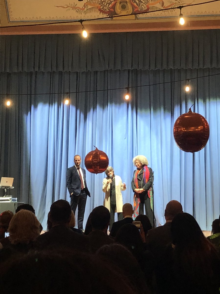 Chesa Boudin, his mother and Angela Davis standing on a stage. His mother has a microphone in her hand