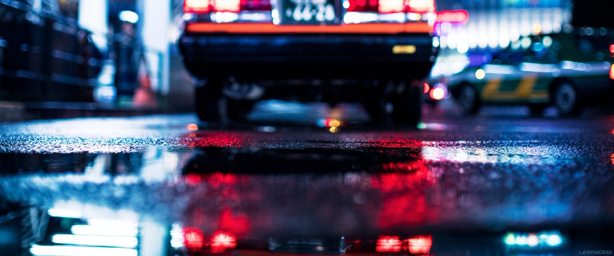 Photography by Liam Wong of Tokyo at night. Captured on a 50mm lens - the focus of this set of images is 'bokeh' and 'rain'. This image focuses on the puddle in front of a taxi which is out of focus.