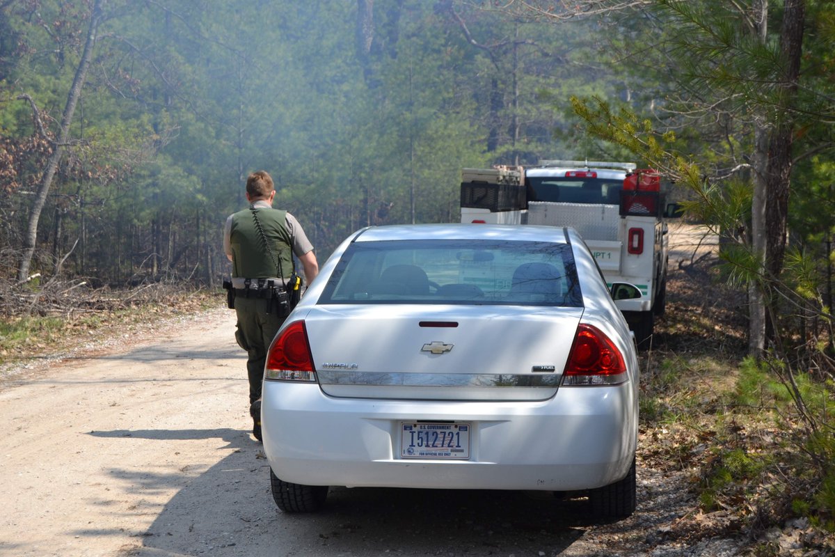 A ranger stands next to a vehicle. In the background is an engine and smoke.
