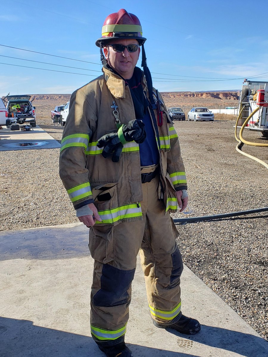 A man in turnout gear stands on pavement.