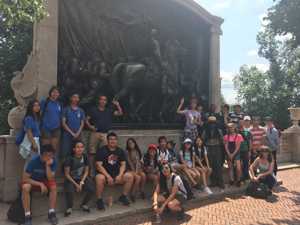 group of teens stand in front of statue 