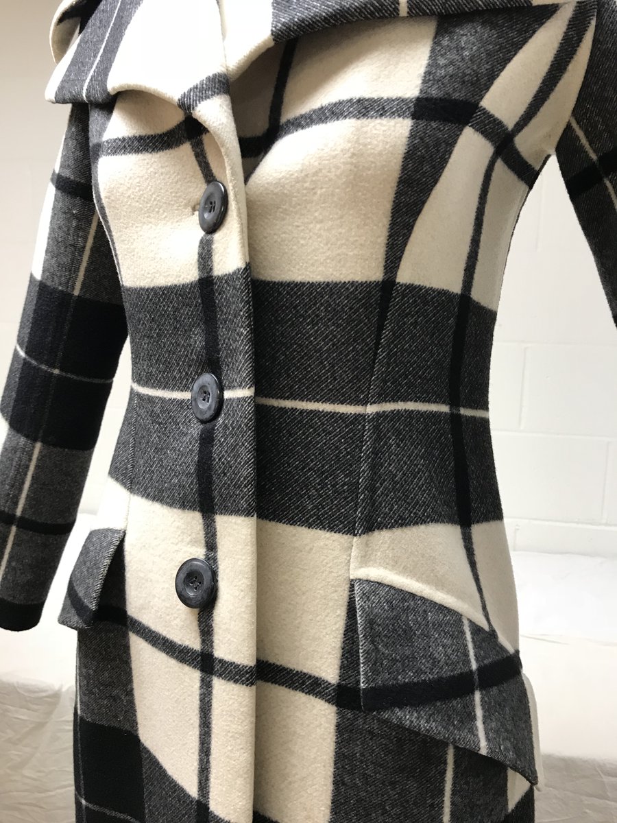 A close-up view of the front of a black and cream plaid coat. There are three buttons and two pockets.
