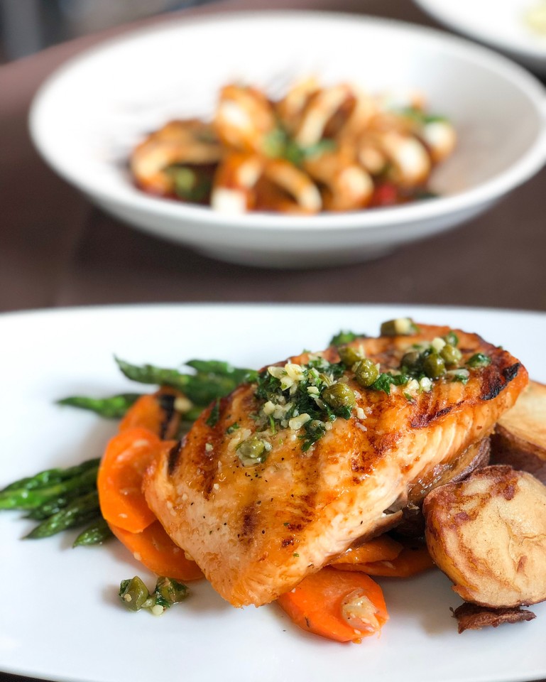 During your next visit, try our Atlantic Salmon. Grilled salmon dressed with capers, olive oil, basil, garlic, served with vegetables. Yum!