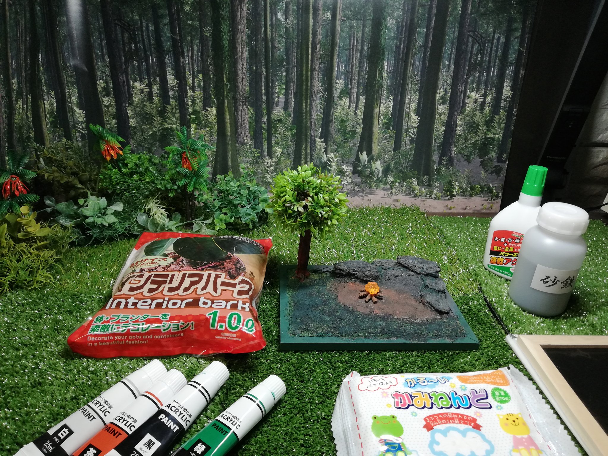 Tori 撮影用100均森です 箱庭技研ジオラマシートを背景に100均の人工芝を敷き造花を設置 中央プチジオラマは紙粘土 インテリアバーク 造花で形作り 電飾埋めて食玩キャンプファイア設置 そして砂鉄を水溶きボンドで接着後に100均アクリルで塗装